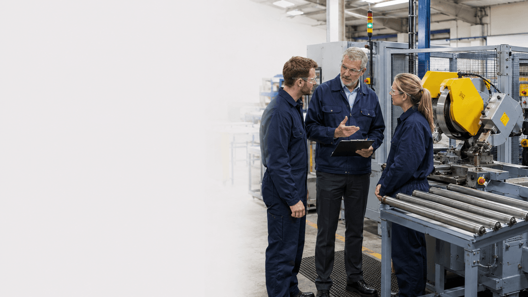 Three workers discuss machinery safeguarding beside industrial equipment for PUWER assessment.